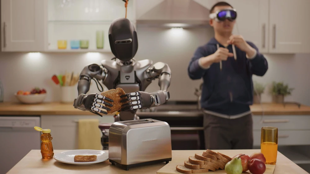 Ein humanoider Roboter in einer Küche wird von einem Mann mit VR-Brille beim Zubereiten eines Toasts gesteuert