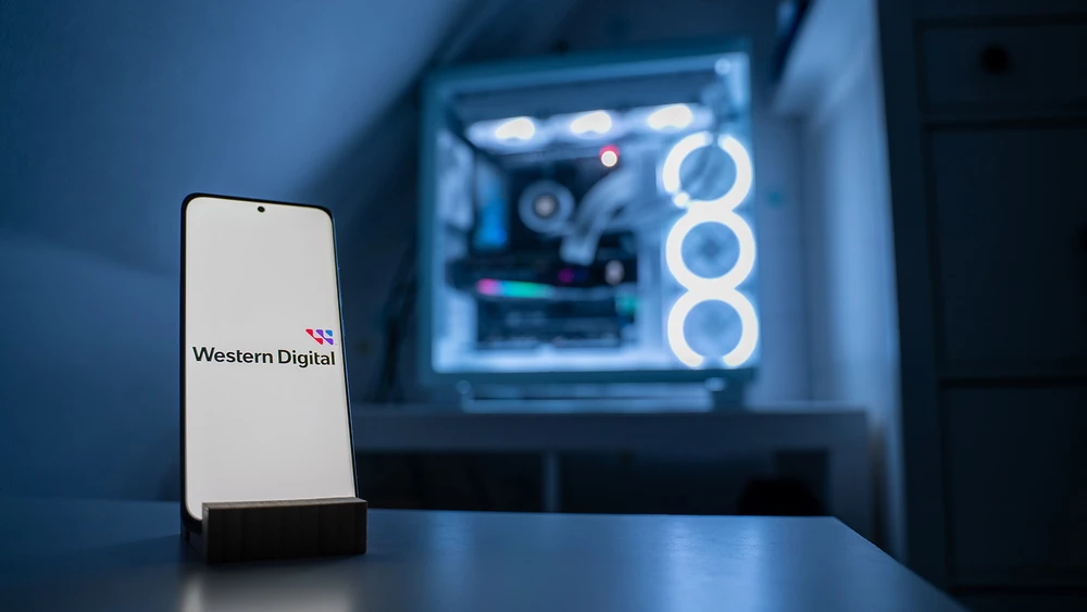 Logo von Western Digital auf Smartphone vor beleuchtetem Gaming-PC