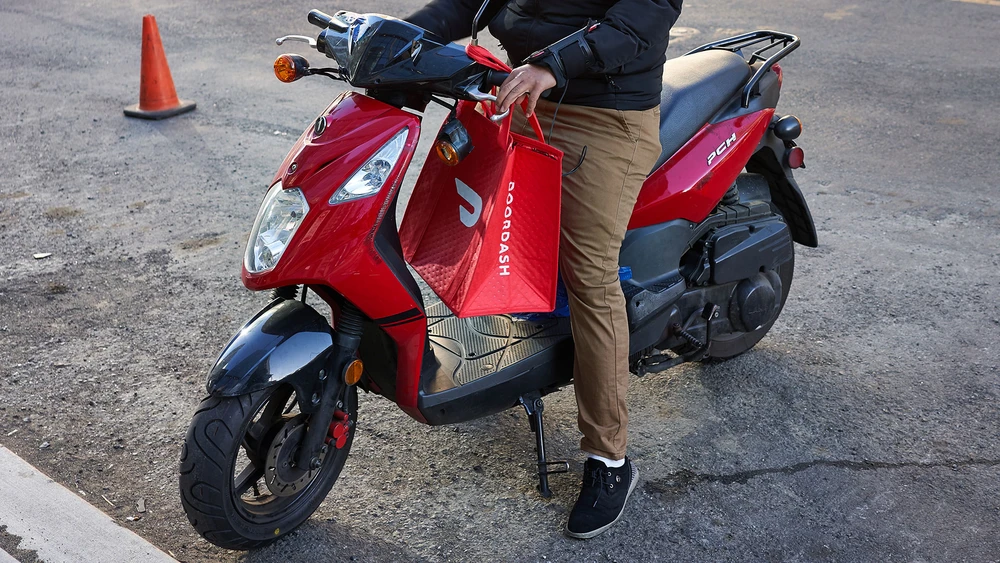 Ein Doordash Lieferant auf einem Motorroller mit Doordash Tüte