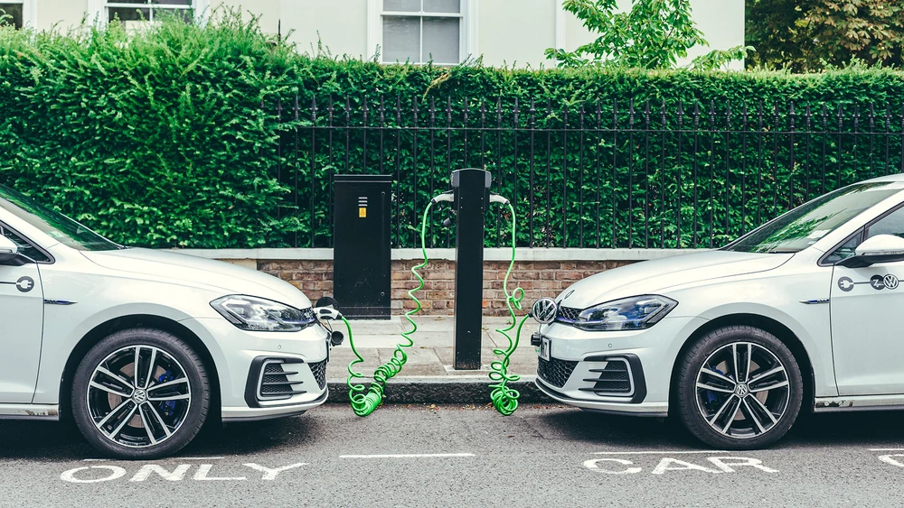 Zwei weiße Volkswagen Golf GTE-Autos laden an einer Ladestation auf einer Straße in London