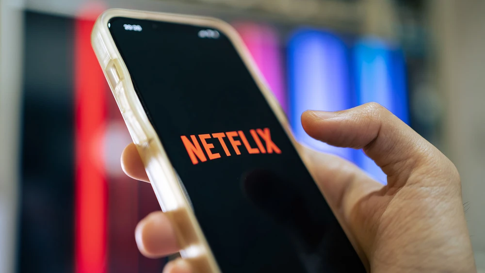 Netflix Logo auf in der Hand gehaltenem Smartphone vor unscharfem Hintergrund