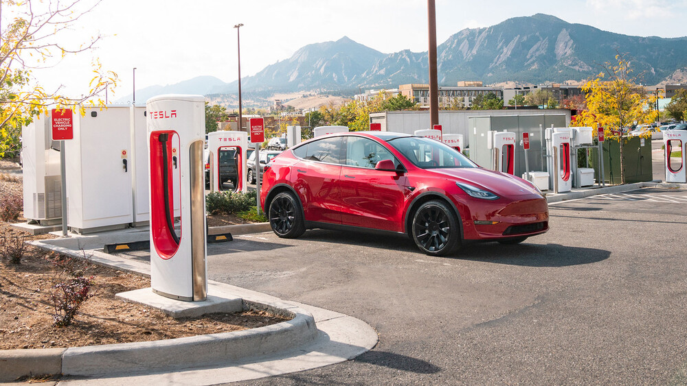 Tesla Model Y in rot steht auf Parkplatz mit Supercharger Ladesäulen